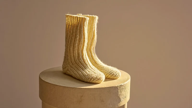 Cremefarbene Wollsocken als skulpturale Anordnung auf einem runden Gipssockel, Illustration