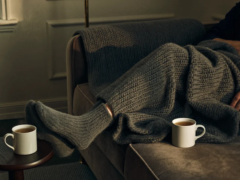 Gemütliche Wohnzimmerecke mit Sofa, Strickdecke und Tee im Abendlicht, Illustration